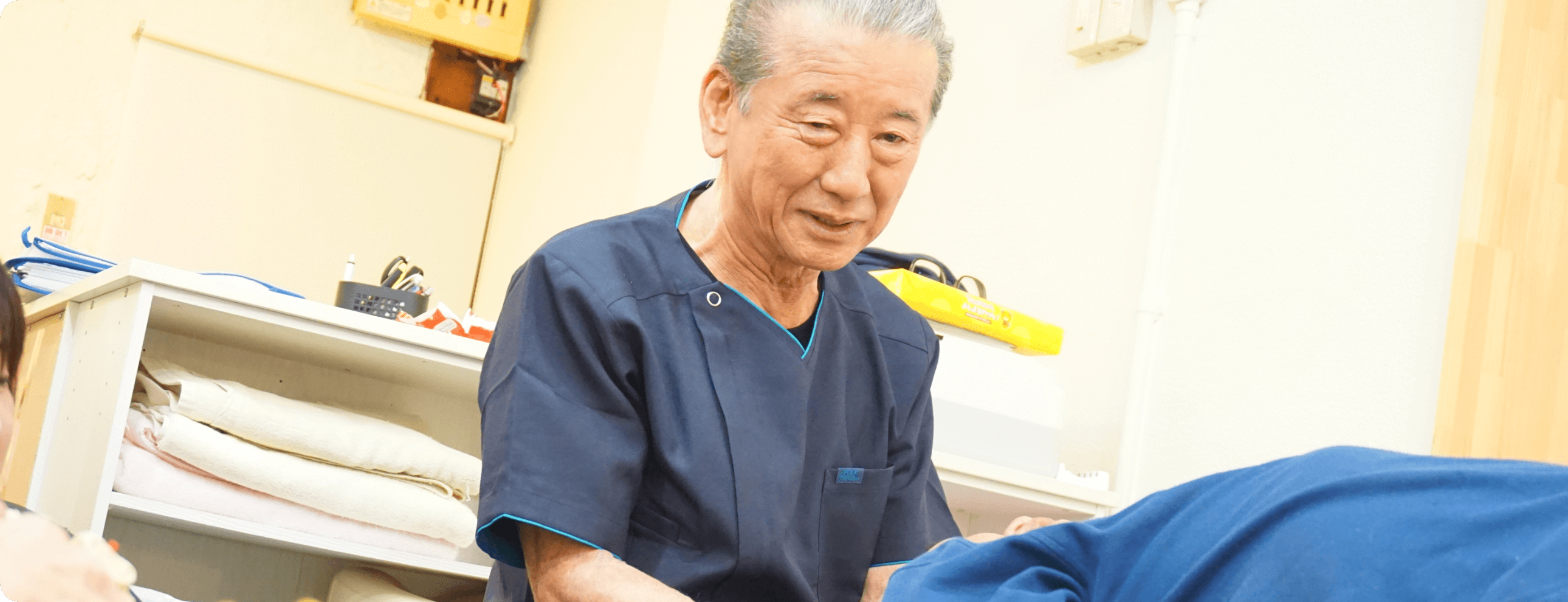 年配の男性施術者が施術着を着て患者の施術を行っている様子の写真