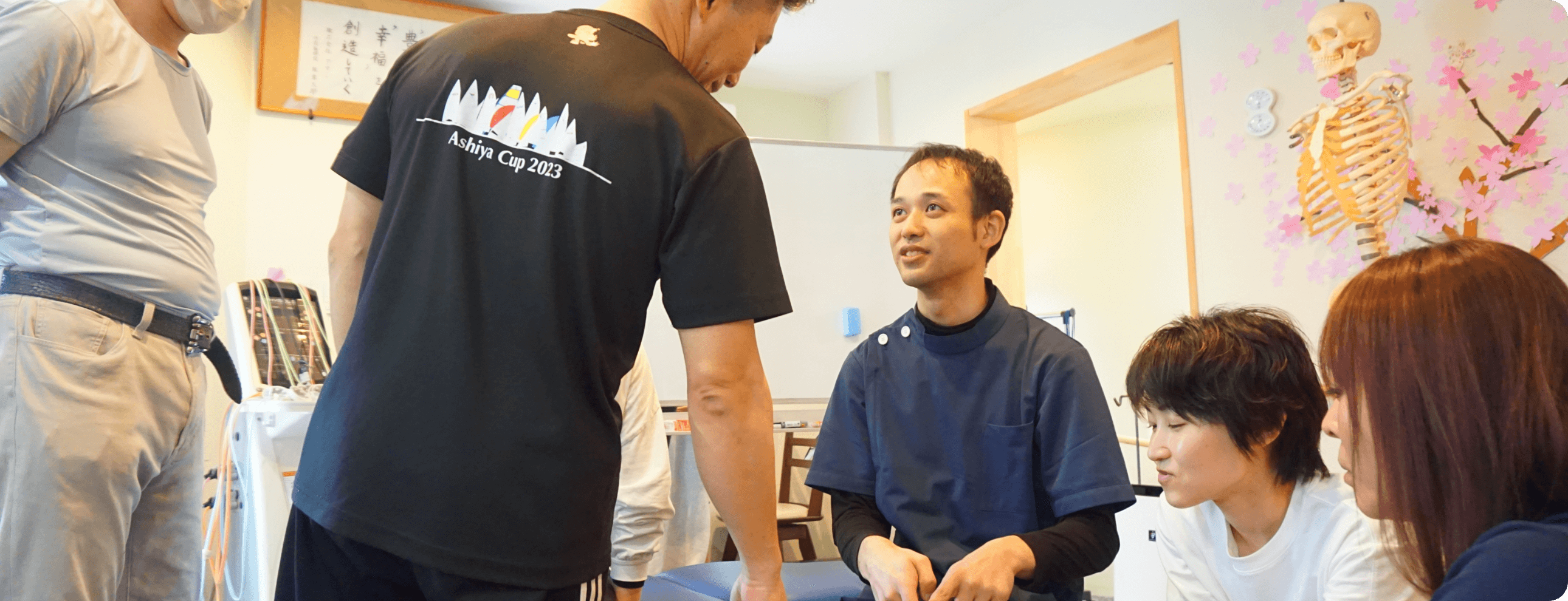 数人の施術者が協力してベッドに横たわる男性の顔や手をケアしている様子