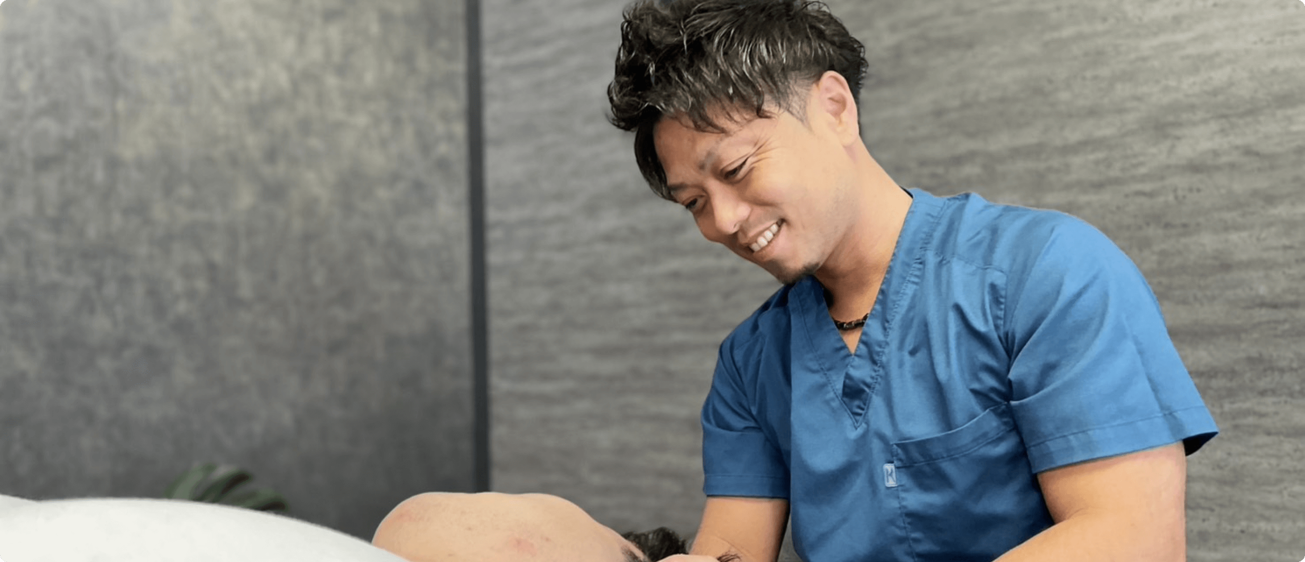 青い施術着を着た男性が笑顔で患者の肩をマッサージしている様子