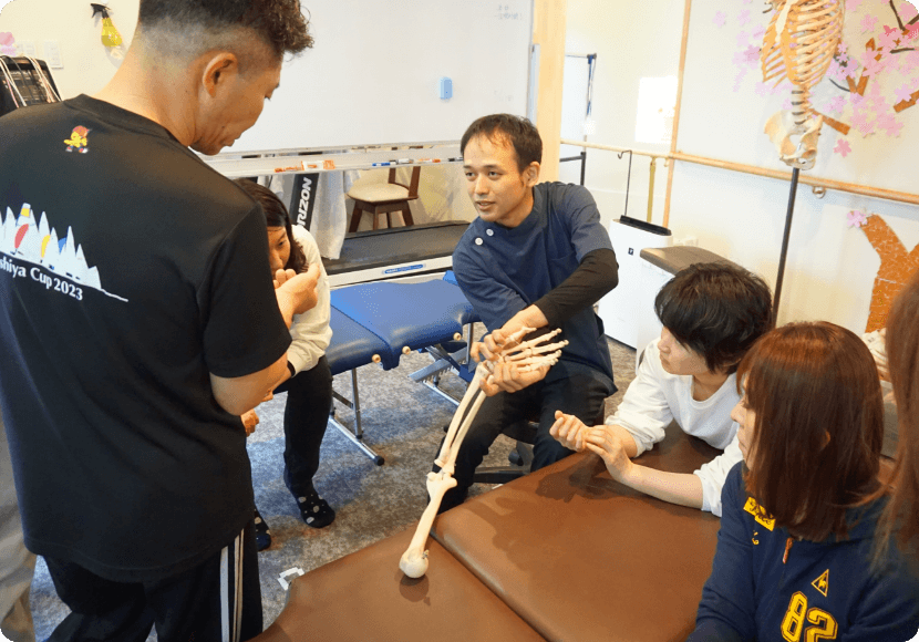 実技指導を受ける様子。複数の生徒が熱心にメモを取りながら聴講している。