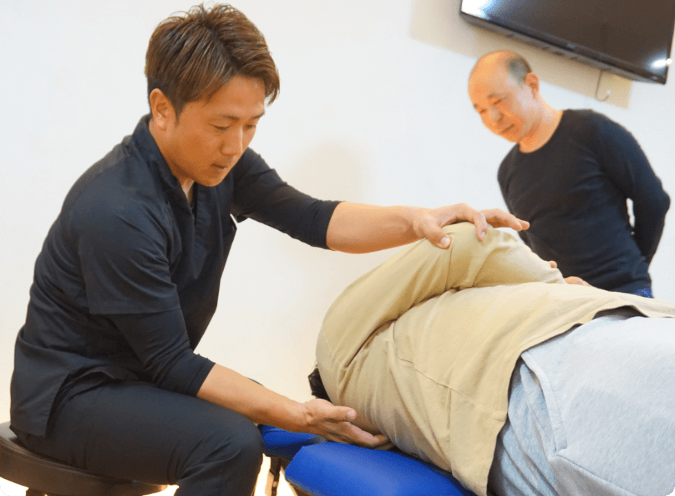 施術者がベッドに横たわる患者の肩と腰を調整している整体の様子を示している
