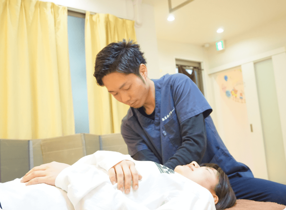 施術者が仰向けになった女性の肩や胸部を押さえて施術している場面を写している